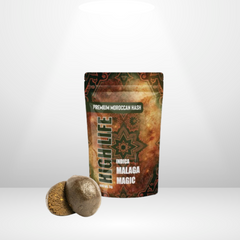 En påse märkt Hero Malaga Magic Indica THCA 5g 40% Hash står upprätt, med två rundade Indica-hashbitar framför, allt mot en vanlig ljus bakgrund.