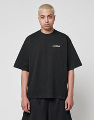 A person with short, bleached blonde hair wears the LIVE FAST DIE YOUNG Basic 280 Tee in black, featuring a small white LiveFast chest print and an oversize fit, paired with black shorts against a plain white background.