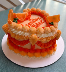 decorated cake with orange buttercream frosting and candied orange wedges, with the text 'A Spritz Older' written on top.