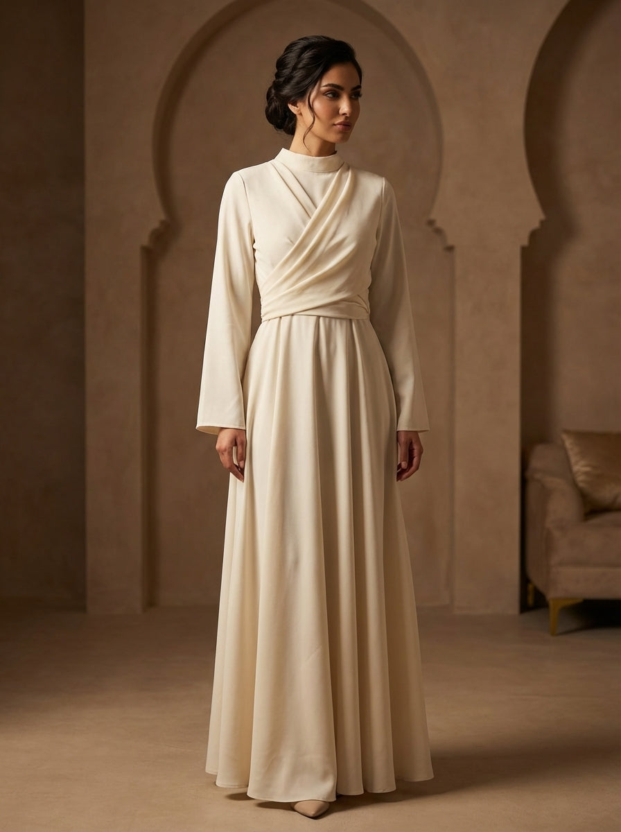 Woman wearing a long, light-colored dress in a warm-toned room with arched doorways.