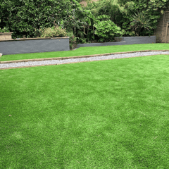 A well-maintained artificial grass lawn with a tree and shrubbery in the background.