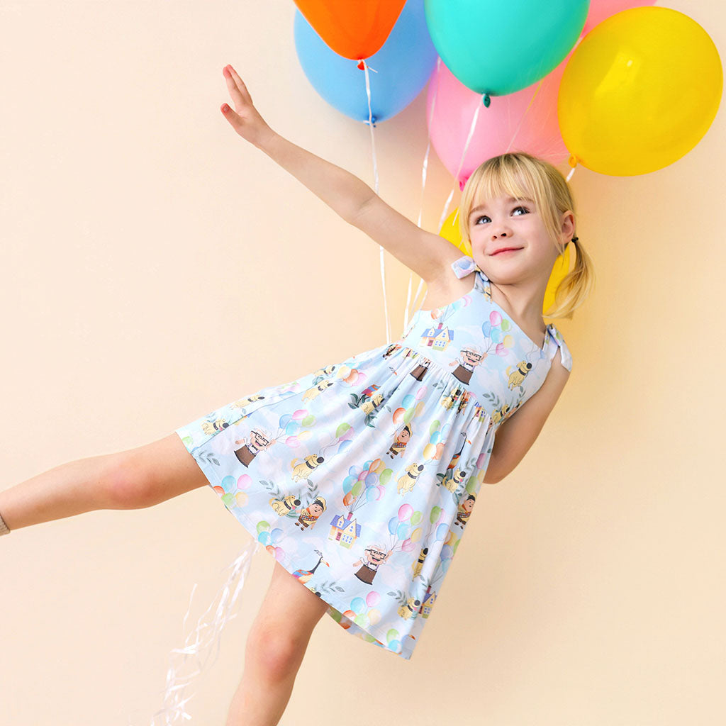 Child in a patterned dress holding colorful balloons against a beige background