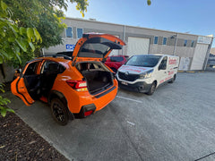 Our team meticulously inspecting a car with the bonnet and doors open, as part of a detailed pre purchase car inspection near Clontarf. Orange SUV with open trunk in a parking lot with a white van in the background.