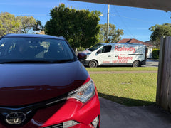 Red car parked on a driveway with a Roadworthy van in the background. An Ausmec Roadworthy Mechanic conducting a comprehensive pre purchase car inspection on a vehicle on the grass at a private seller's home in Clontarf.