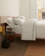 image 4 of 5 showing Rise & Fall's Soft & Smooth duvet set in bedroom setting, colour: white with navy piping, fabric: sateen cotton