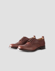 A pair of brown leather brogues with heel pull detail and contrast leather lining. Side angle flat lay view.