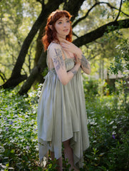 Woman wearing a flowing Flutter Fairy Dress with handkerchief hem standing in a sunlit forest clearing.