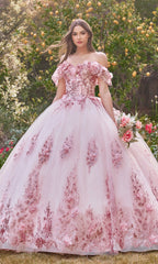 A woman stands outdoors in a garden wearing the Glitter Quince Dress with Back Bow: Ladivine 15701, a pink, off-the-shoulder ball gown with floral embroidery, holding a bouquet—an enchanting look perfect for a quinceañera.