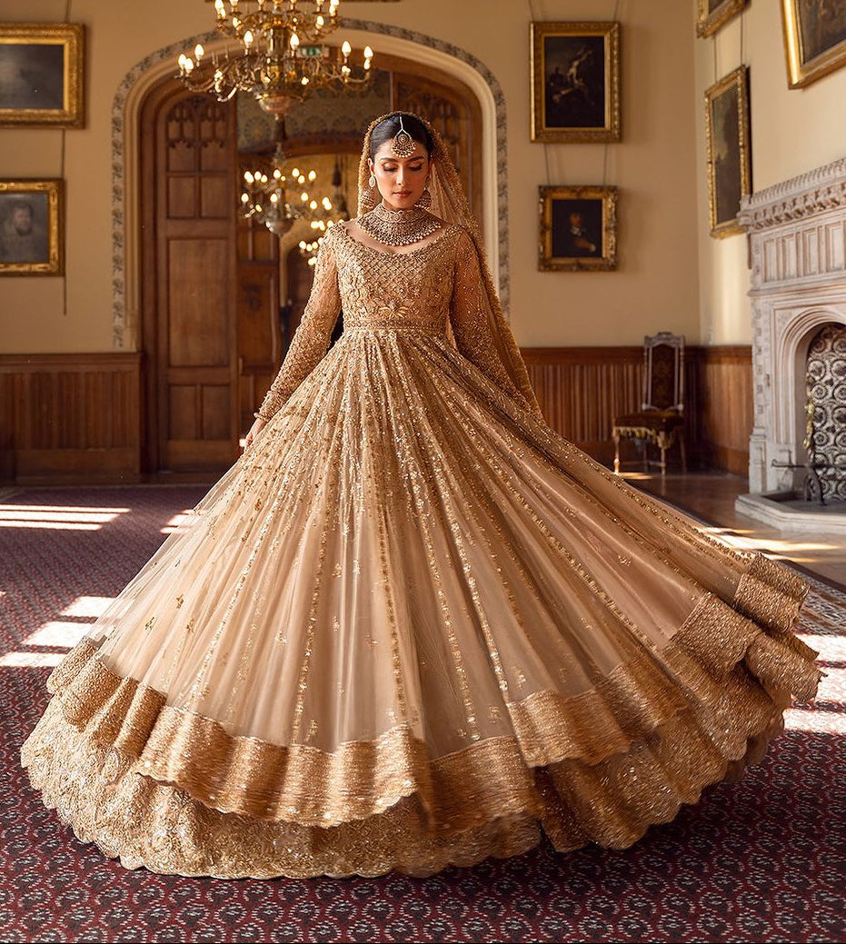 Ayeza Khan famous Pakistani actress in a traditional golden gown with embellishments and a dupatta stands in a room with historical paintings.