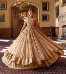 Ayeza Khan famous Pakistani actress in a traditional golden gown with embellishments and a dupatta stands in a room with historical paintings.
