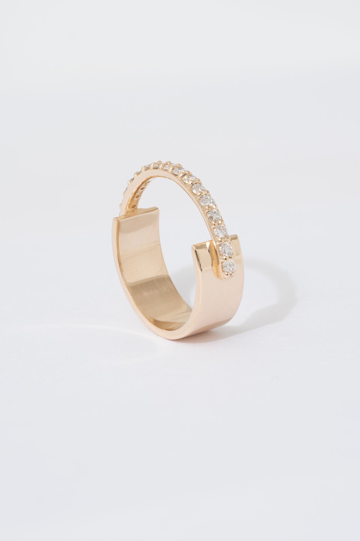 A gold ring with a flat wide backing and a single row of pave white diamonds around the front half of the band, displayed against a white background.