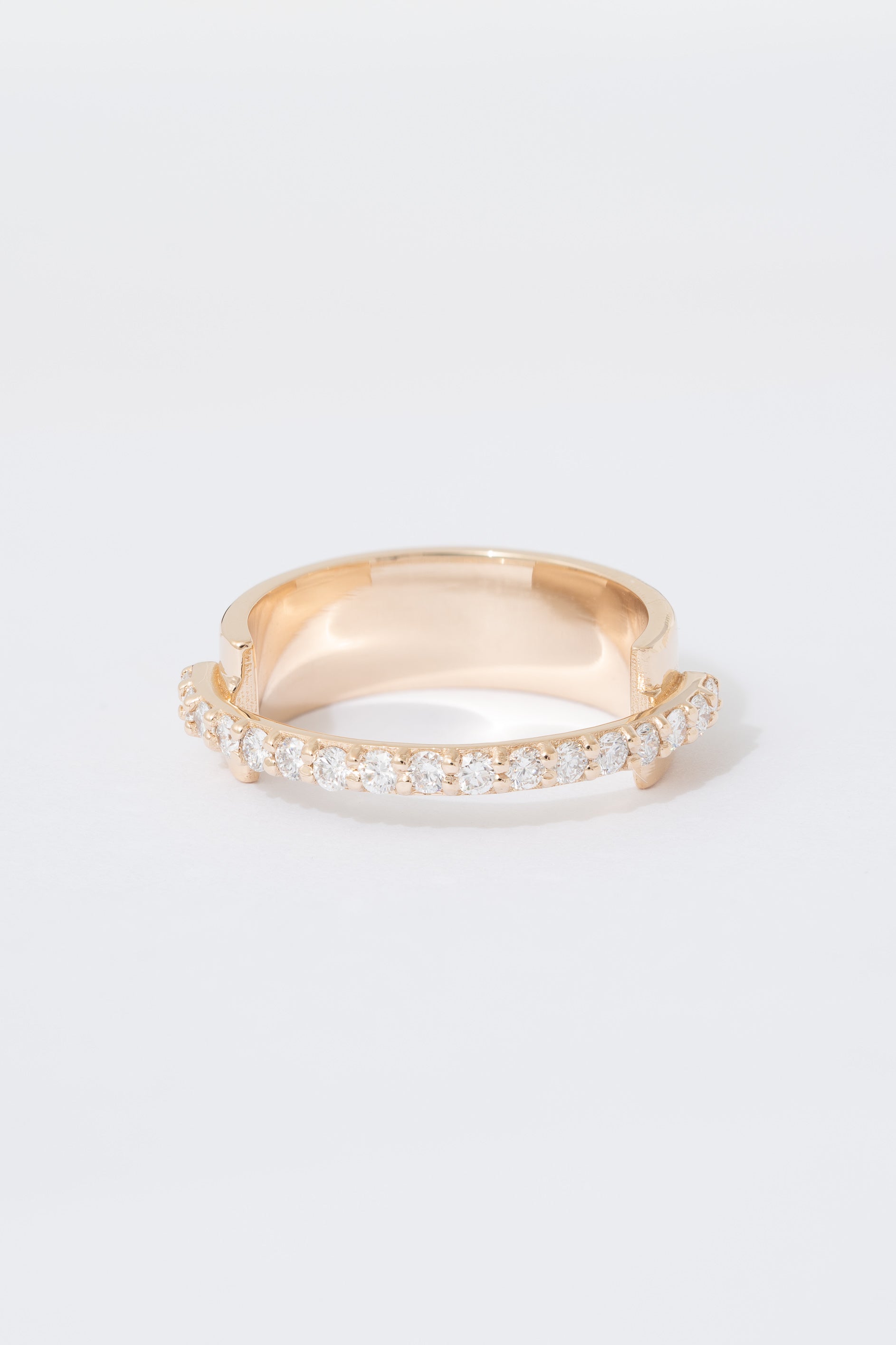A gold ring with a flat wide backing and a single row of pave white diamonds around the front half of the band, displayed against a white background.