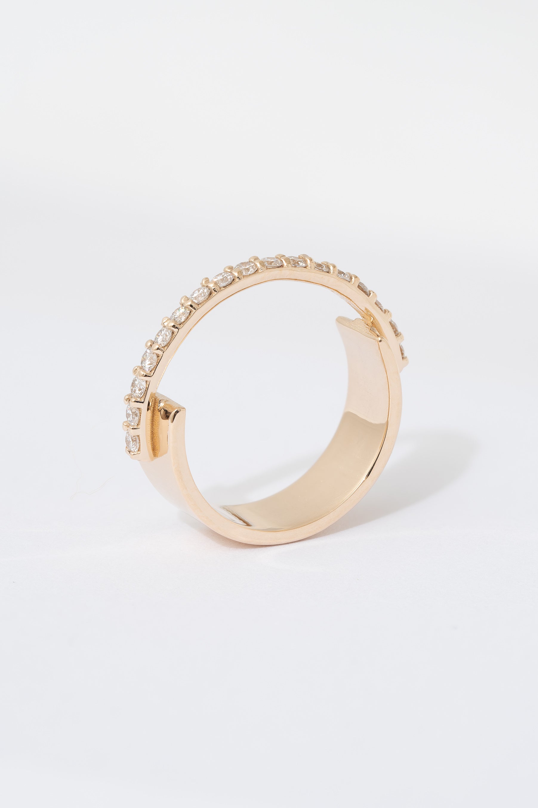 A gold ring with a flat wide backing and a single row of pave white diamonds around the front half of the band, displayed against a white background.