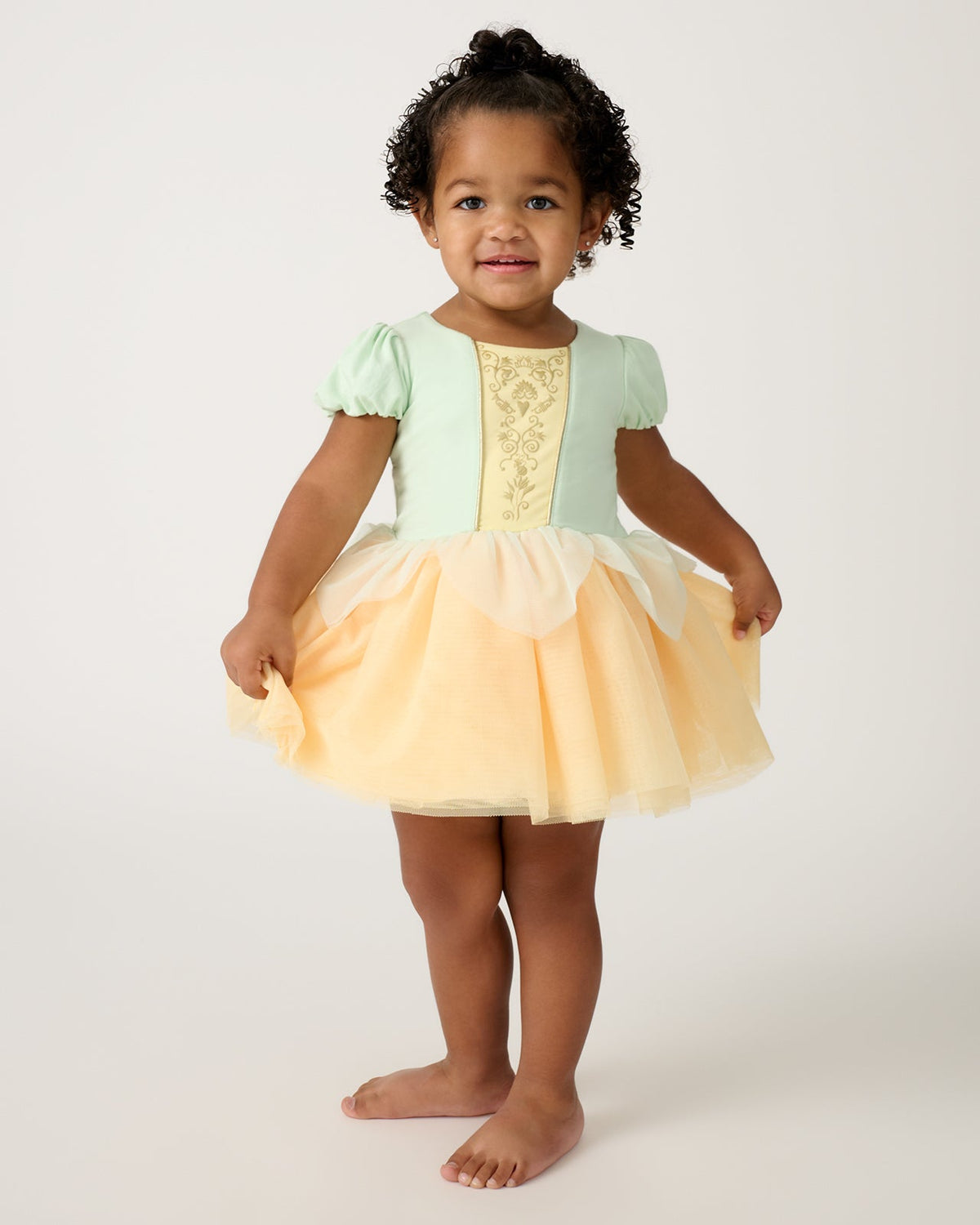 Standing toddler wearing the Disney Princess Tiana Dress with Bodysuit