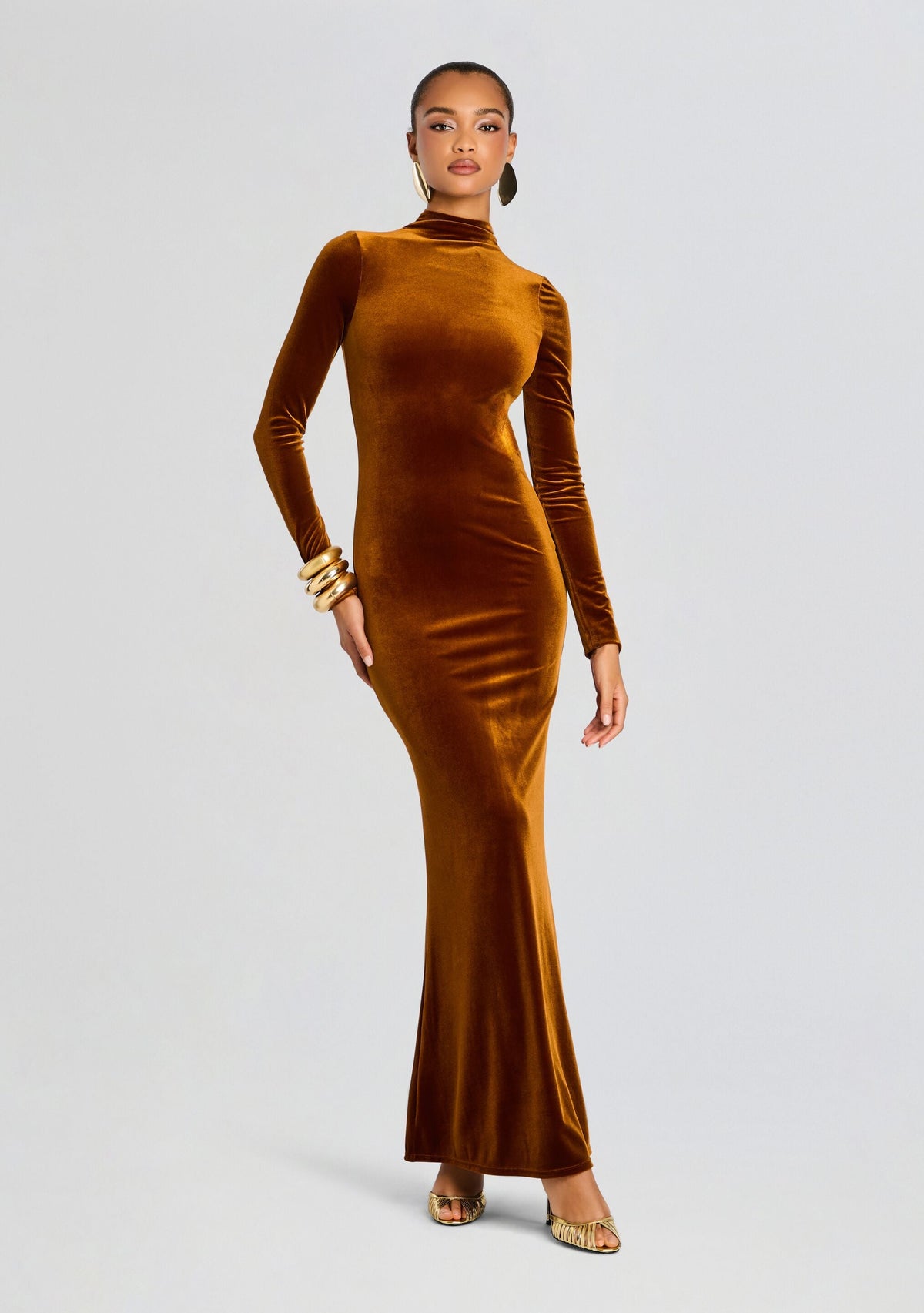 Full length shot of a model in a burnt orange velvet maxi dress with long sleeves and a high neckline