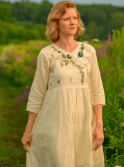 Woman wearing a cream-colored dress with floral embroidery standing in a field of flowers.
