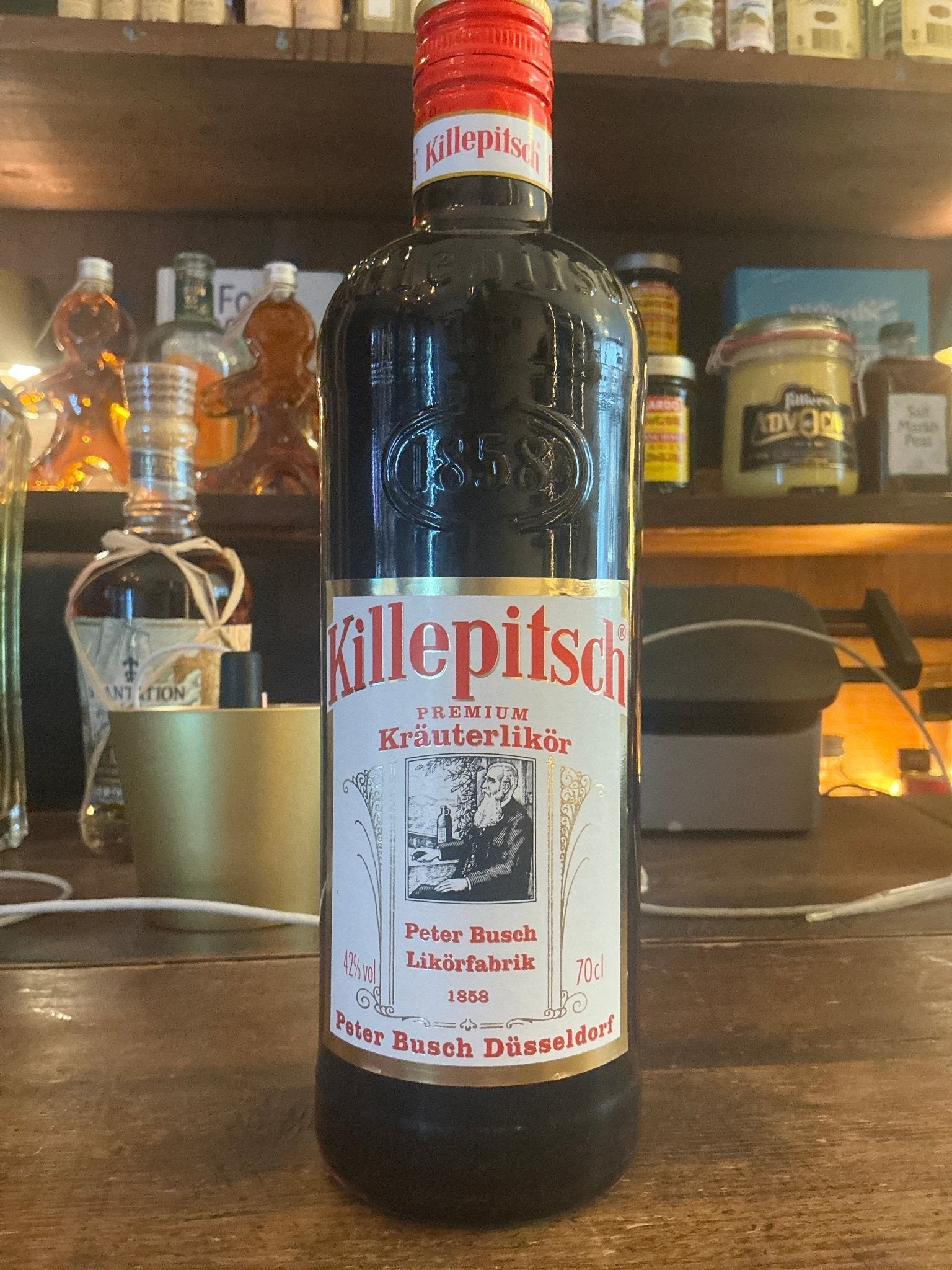 Killepitsch herbal liqueur bottle with red cap, botanical spiced premium small batch specialty spirit on wooden bar counter.