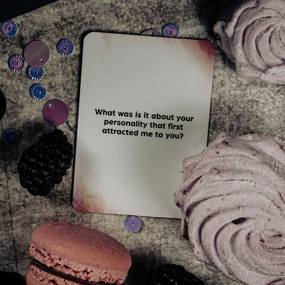 Ett kort från "Box Of Burning Desires" frågar efter personlighetens attraktion bland björnbär, macaron och maräng på en strukturerad yta, vilket inbjuder till intimitet och romantik.